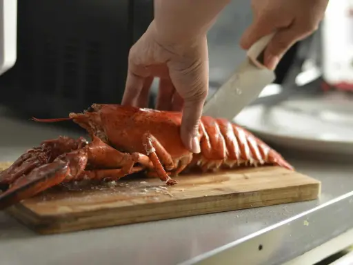 Hand schneidet gekochten Hummer für ein Hummer-Rezept auf einem Holzbrett.