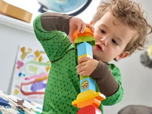 Niño concentrado armando una torre con bloques de colores, ideal para juguetes por edades.