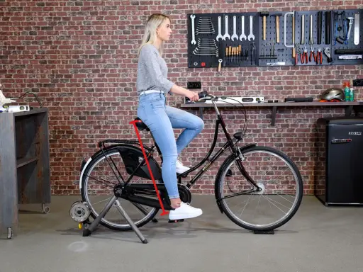 Frau sitzt auf einem Fahrrad auf einem Rollentrainer. Ein roter Pfeil zeigt die richtige Höhe des Fahrradsattels an, um den Fahrradsattel richtig einzustellen.