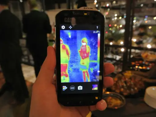 Ręka trzyma smartfon Cat S60 z włączoną termowizją, pokazującą dwie osoby w cieplejszych barwach.