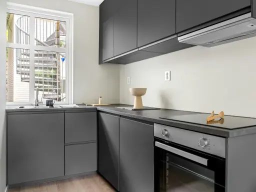 Diseño cocina restaurante moderno con gabinetes grises, encimera oscura y ventana con escalera exterior.