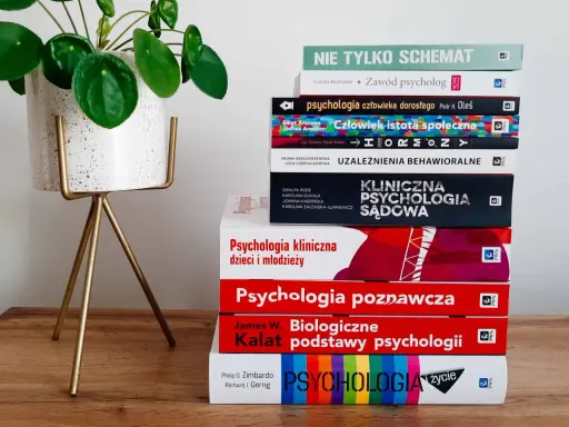 Książki o psychologii, w tym "Biologiczne podstawy psychologii" Kalata, na drewnianym tle obok rośliny.