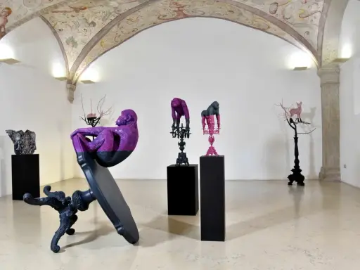 Sculture di scimmie e cervi colorati, opere di **artisti contemporanei famosi**, in una galleria con affreschi sul soffitto.