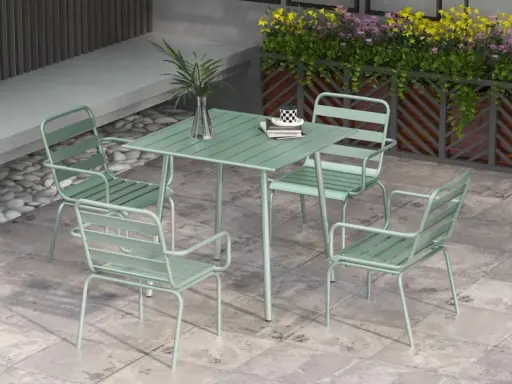 En grön rottingfåtölj utomhus, del av ett cafébord med stolar.