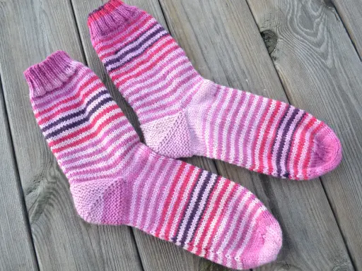 Två par randiga sockor i rosa och lila toner ligger på en träyta.