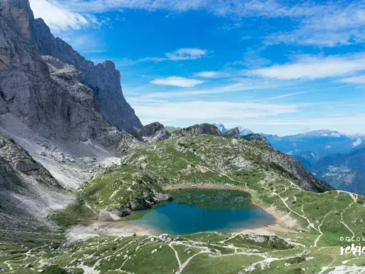 Lago di Coldai, incastonato tra le maestose vette delle Dolomiti, con sentieri che si snodano sui prati verdi.