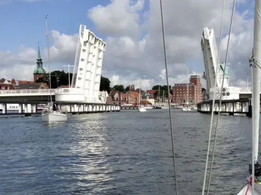 Eine Klappbrücke öffnet sich für Segelboote in Kappeln an der Schlei. Im Hintergrund die Stadt mit Kirchturm und Backsteingebäuden.