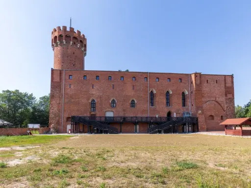 Zamek w Świeciu, ceglana twierdza z wieżą, otoczona zielenią i dziedzińcem.