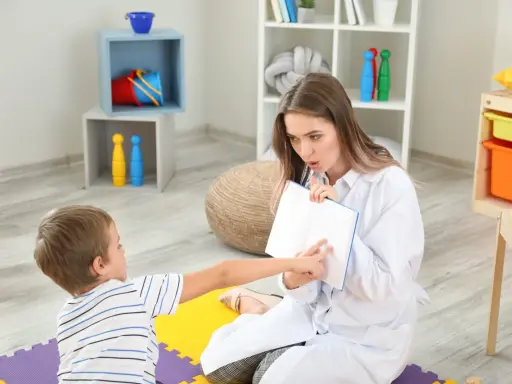 Terapeuta pracuje z dzieckiem nad poprawą niewyraźnej mowy, wskazując palcem na strony otwartej książki.