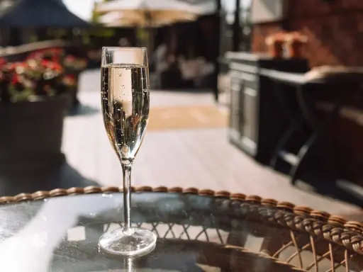 Ein Glas Sekt auf einem Tisch im Freien. Die Bläschen im Glas zeigen, dass der Sekt frisch ist und die Haltbarkeit noch gut ist.