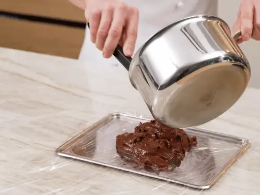 Comment faire fondre du chocolat : une casserole verse du chocolat fondu sur une plaque recouverte de film plastique.