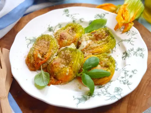 Deliziosi fiori di zucca al forno, ripieni e dorati, guarniti con basilico fresco su un piatto decorato.