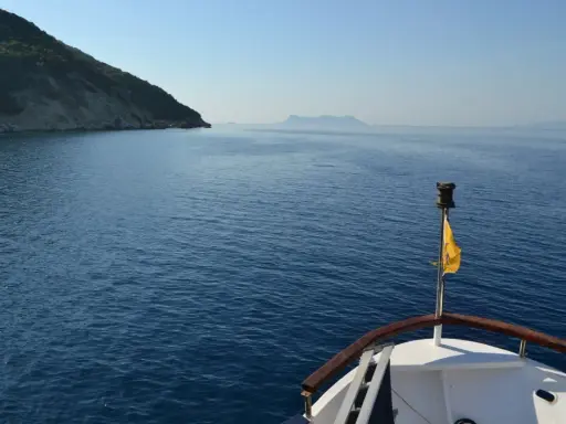 La prua di una barca naviga verso un'isola lontana, un viaggio che evoca la poesia di Itaca.
