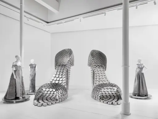 Installazione artistica mostra valentino roma: due enormi scarpe metalliche e abiti da sera su manichini.