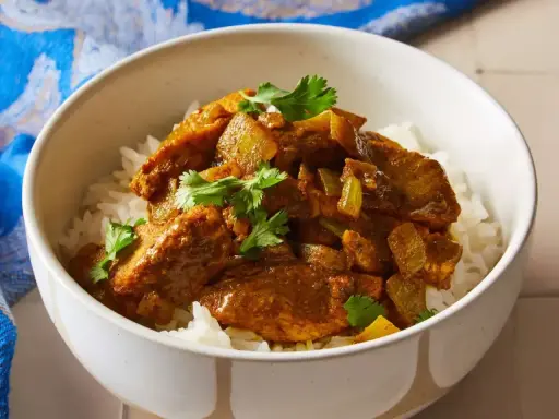 Aksamitny kurczak w sosie curry, podany na białym ryżu, z gałązkami kolendry. Idealny prosty przepis na obiad.