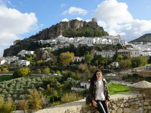 Una mujer sonríe ante el pintoresco pueblo blanco de la sierra de Cádiz, coronado por un castillo.