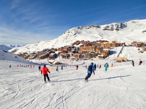 Ośrodek narciarski we francuskich Alpach. Tłumy narciarzy i snowboardzistów na stoku, w tle zabudowania. Francja narty gdzie najlepiej? Tutaj!