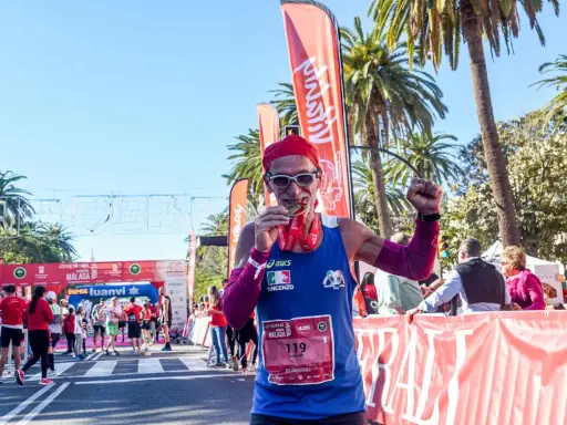 Lächelnder Läufer mit Medaille und rotem Kopftuch feiert seinen Erfolg beim Malaga Marathon.