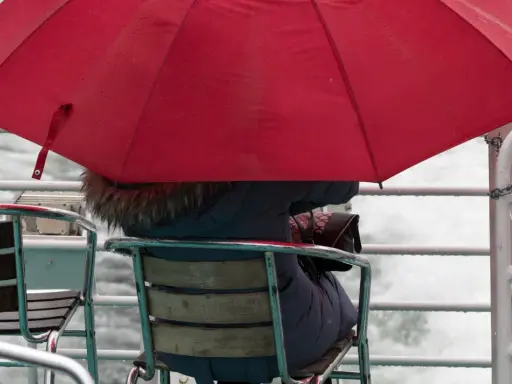 Person under röd paraply på en båt, omgiven av brusande vatten. En typisk bild av bergen regndagar.
