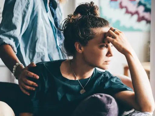 Una donna pensierosa, con una mano sulla fronte, riceve un gesto di conforto. Potrebbe riflettere sull'attaccamento evitante e la sessualità.
