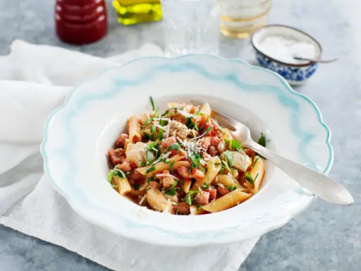 En tallrik med penne pasta, kyckling och tärnad pancetta, toppad med persilja och parmesan. Ett enkelt pancetta recept för en god middag.