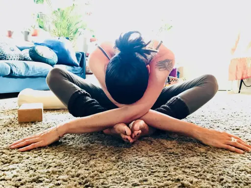 En kvinna i en djup yogaställning på en fluffig matta, omfamnar sig själv i en gest av nonduality.