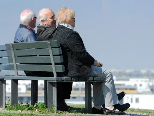 Trzech seniorów siedzi na ławce, rozmawiając. Może to dyskusja o tym, czym jest emerytura pomostowa i jakie daje możliwości.