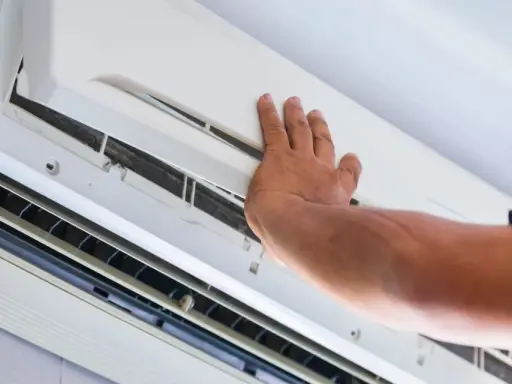 Main d'un technicien ouvrant un climatiseur pour vérifier l'eau et le filtre.