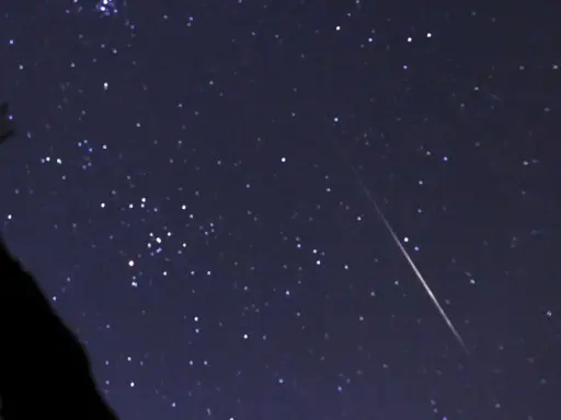 En stjärnklar natt med en meteor som drar en ljusstrimma över himlen, ett av många olika ljusfenomen på himlen.