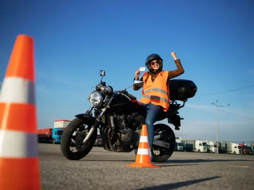 Szczęśliwa motocyklistka z prawem jazdy kategorii A3 w ręku, siedząca na motocyklu, świętuje sukces na placu manewrowym.