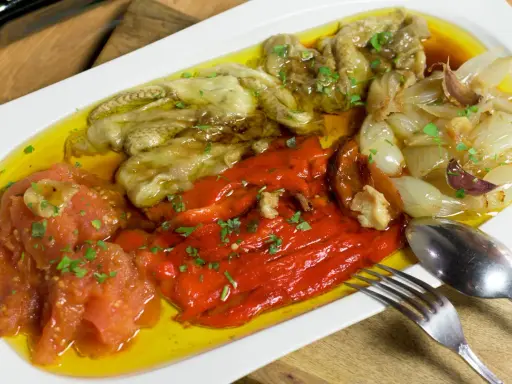 Deliciosa escalivada al forn con pimientos rojos, berenjenas, tomates y cebollas asadas, regada con aceite de oliva y perejil picado.
