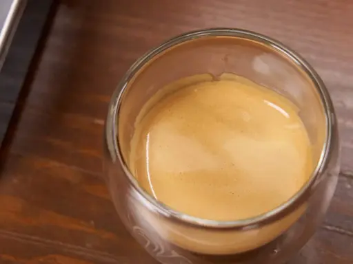 Ein Glas Espresso mit einer feinen Crema auf einem Holztisch. Ein kleiner Schuss Sahne macht den Kaffee mit Sahne gesund und lecker.