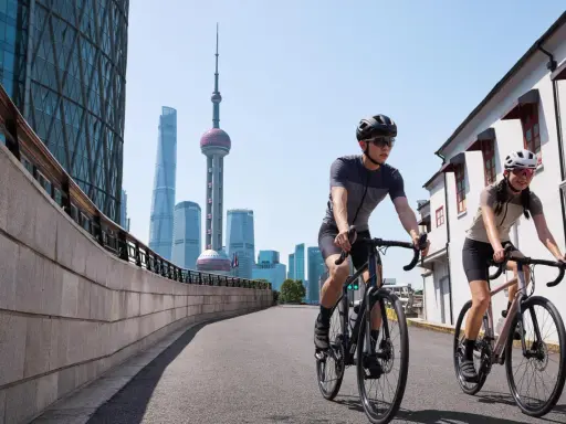 Dwóch rowerzystów w kaskach przemierza miasto, mijając nowoczesne wieżowce i tradycyjną architekturę. Różne rodzaje bębenków rowerowych pozwalają na płynną jazdę.