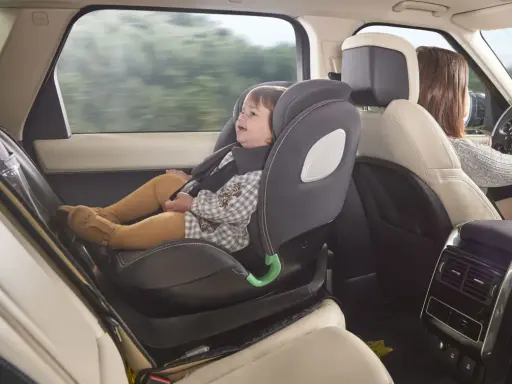 Bebé sonriente en silla de coche a contramarcha, viajando segura mientras mamá conduce.
