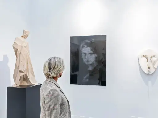 A woman views a collection of art, including a wooden sculpture and a portrait, appreciating art as an asset class.