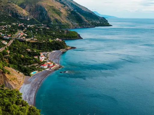 Villaggio costiero con case bianche e rosse affacciato su una spiaggia di ciottoli scuri e mare blu intenso. Le **basilicata spiagge** offrono panorami mozzafiato.