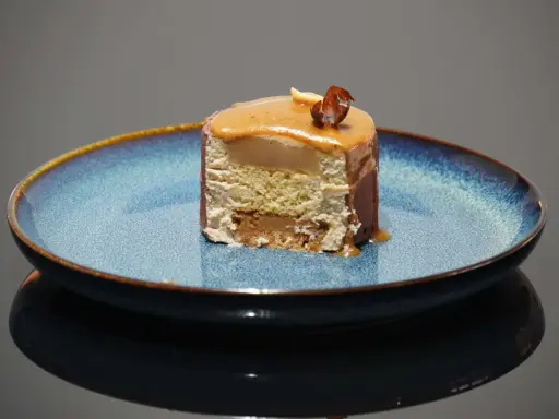 Tranche d'entremet aux couches aériennes, surmontée d'un glaçage caramel et d'une noisette croquante. Le biscuit noisette pour entremet offre une texture légère et savoureuse.