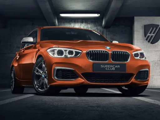 Pomarańczowe BMW 140i z tabliczką "SUPERCAR CLUB" stoi w garażu.