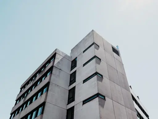 Betonowy budynek o geometrycznej bryle, z rzędami okien. Ta kategoria obiektu budowlanego dominuje w kadrze.