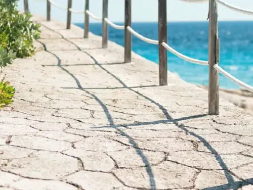 Camino de piedra con barandilla y mar azul. Un ejemplo de cómo hacer hormigón impreso para exteriores.