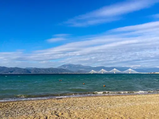 Spokojne morze i plaża w Grecji w styczniu. W oddali widać most Rio-Antirio i góry.