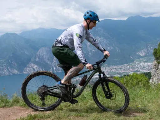 Mężczyzna w kasku jedzie na rowerze MTB po górskim szlaku. Widok na jezioro i miasto w oddali.