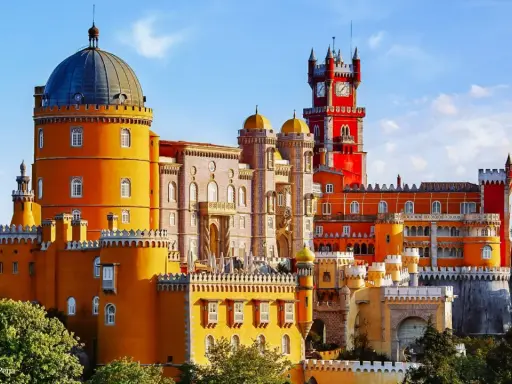 Buntes Sintra Pena Palace mit gelben und roten Türmen, einer blauen Kuppel und einem Uhrenturm unter blauem Himmel.