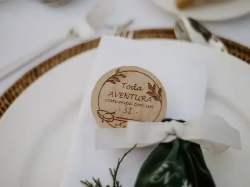 Detalle de mesa de boda con un distintivo de madera que dice "Toda aventura comienza con un SÍ". Ideas para nombres de mesas de boda.