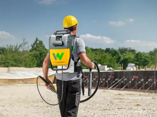 Bauarbeiter mit Rucksackeinheit und Rüttler zur Beton verdichten auf einer Baustelle.