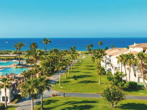 Traumhafter Blick auf das Granada Meer, Palmen säumen den Weg zum Pool und den weißen Hotelgebäuden.