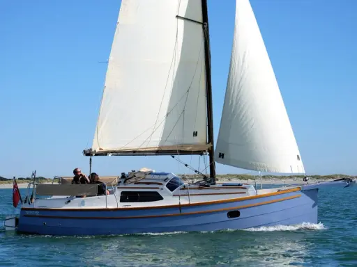 Eine blaue Baycruiser 26 segelt auf ruhigem Wasser unter klarem Himmel. Zwei Personen genießen die Fahrt.