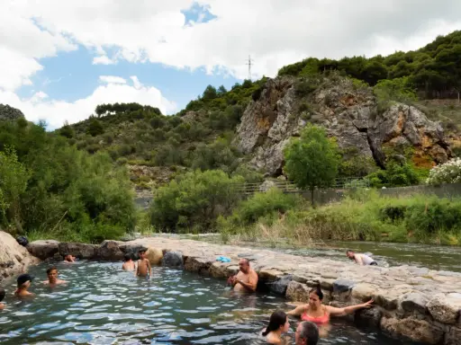 Gente disfrutando de las piscinas naturales en La Rioja, rodeadas de vegetación y rocas.
