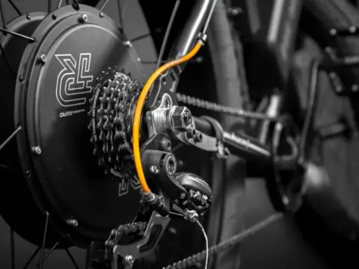 Zestaw do konwersji roweru: czarna piasta z logo, kasetka Shimano, pomarańczowy przewód i przerzutka.