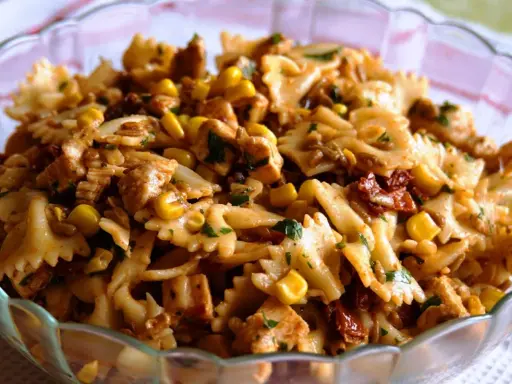 Pyszna sałatka z kurczakiem i makaronem farfalle, kukurydzą i suszonymi pomidorami, posypana natką pietruszki.